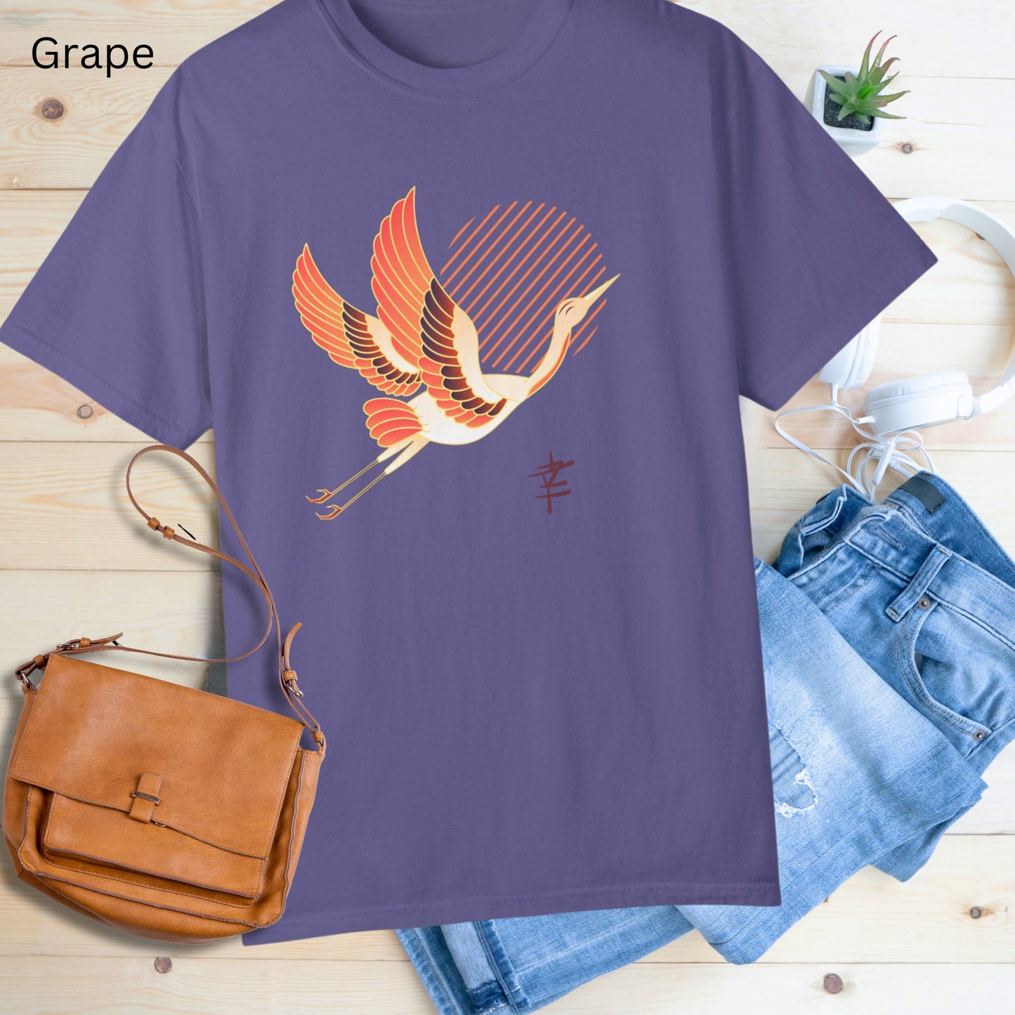 Crew neck purple short sleeve T-shirt with a white and orange japanese crane  flying with legs extended behind it in front of diagonal orange lines arranged to make a sun in the middle. Japanese kanji symbol for happiness below the crane on the left.