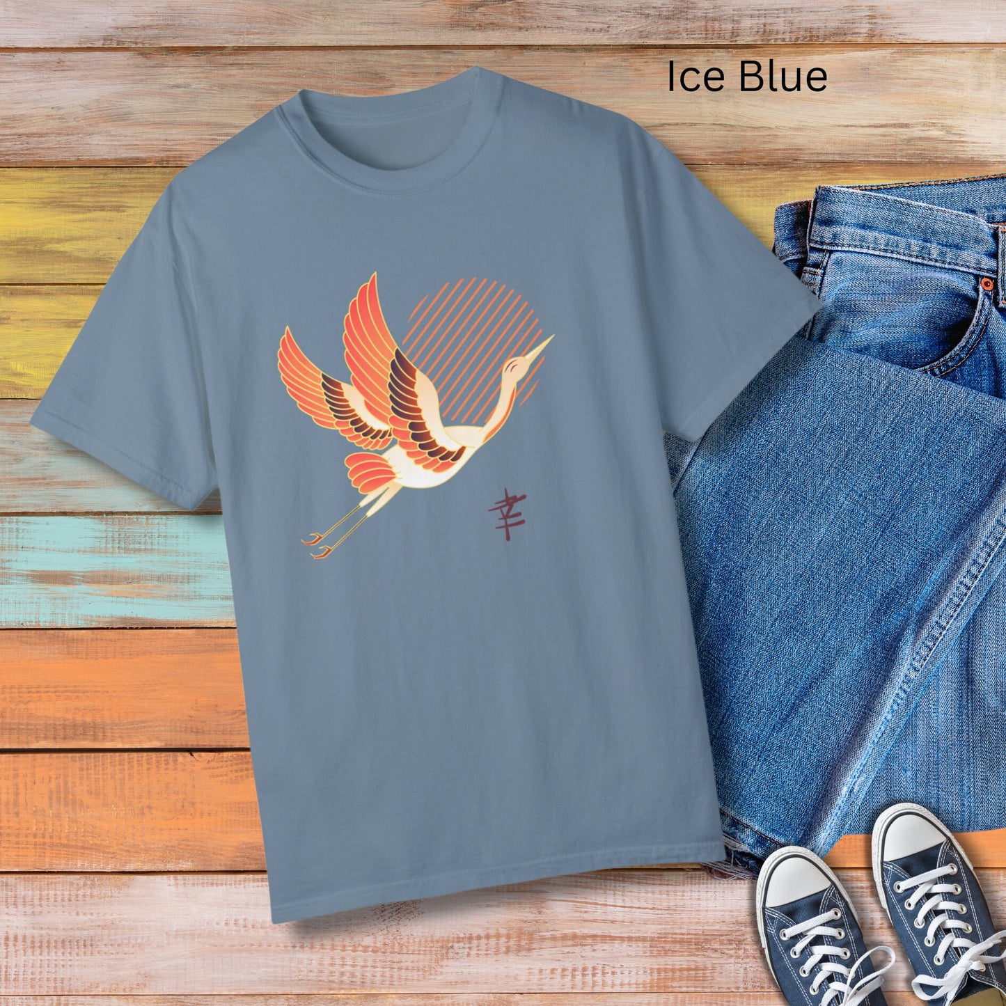 Crew neck blue short sleeve T-shirt with a white and orange japanese crane  flying with legs extended behind it in front of diagonal orange lines arranged to make a sun in the middle. Japanese kanji symbol for happiness below the crane on the left.