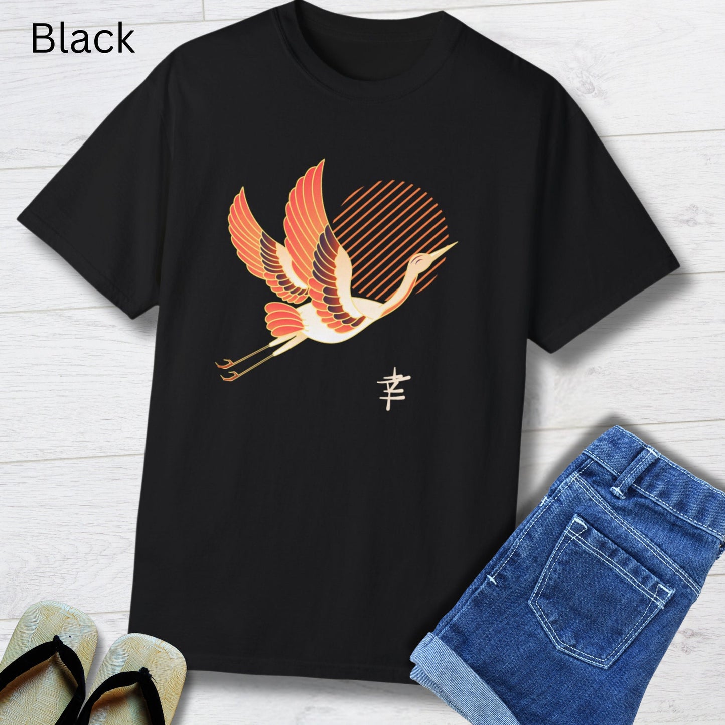 Crew neck black short sleeve T-shirt with a white and orange japanese crane  flying with legs extended behind it in front of diagonal orange lines arranged to make a sun in the middle. Japanese kanji symbol for happiness below the crane on the left.